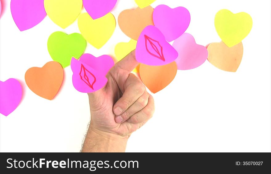 Man's hand with paper labels in the form of hearts on the thumb and forefinger on the background of the lot of labels in the form of hearts. Drawn lips merge in a kiss. Man's hand with paper labels in the form of hearts on the thumb and forefinger on the background of the lot of labels in the form of hearts. Drawn lips merge in a kiss