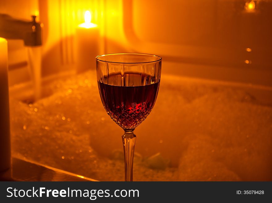 A glass of red wine by candle light and a bubble bath. A glass of red wine by candle light and a bubble bath