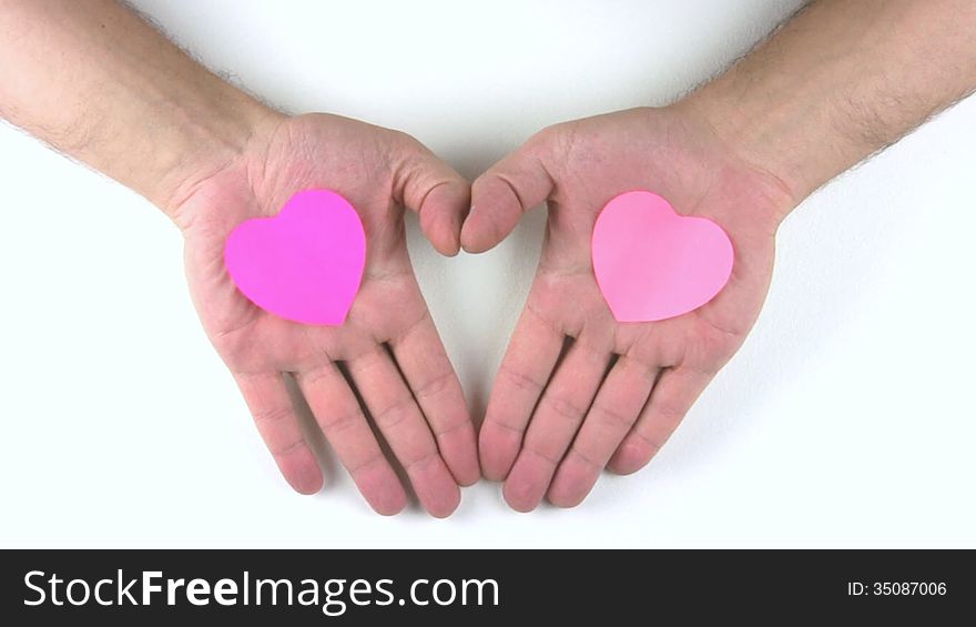 A person's palm with a pink heart-shaped stickers to reveal a white background and thumb form a third heart. A person's palm with a pink heart-shaped stickers to reveal a white background and thumb form a third heart