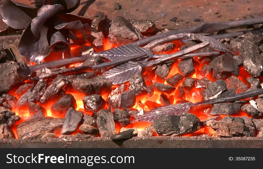 Over the furnace with bright red embers quivering hot air. In the hearth are forged components for metallic flower, and next - finished metal flower. Art of blacksmiths