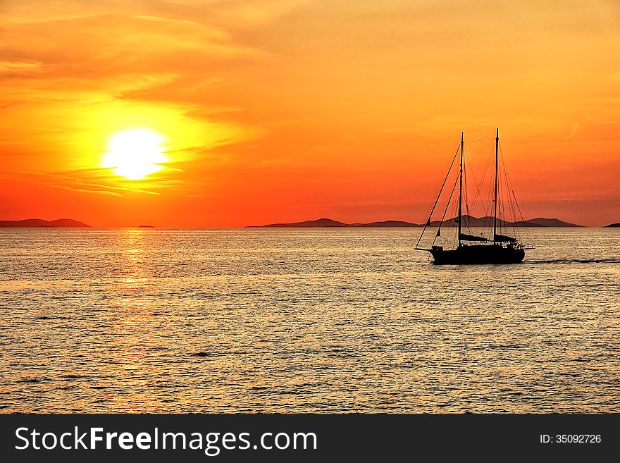 Sunset above the calm sea with sailboat