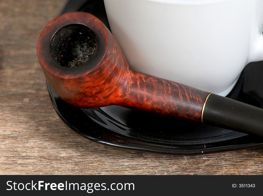 An image of pipe and white cup on saucer. An image of pipe and white cup on saucer