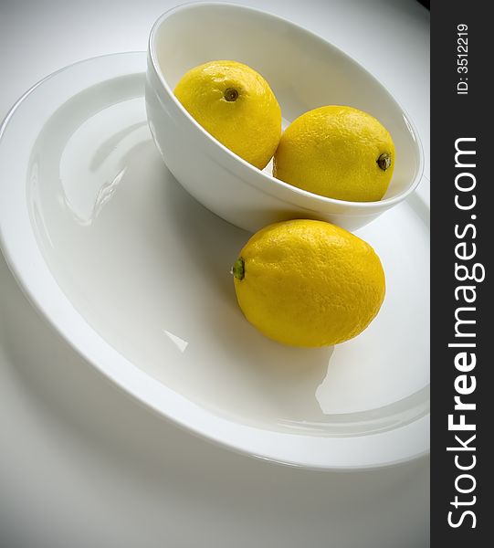 3 lemons. 2 in a bowl, 1 on a plate tilted view. 3 lemons. 2 in a bowl, 1 on a plate tilted view