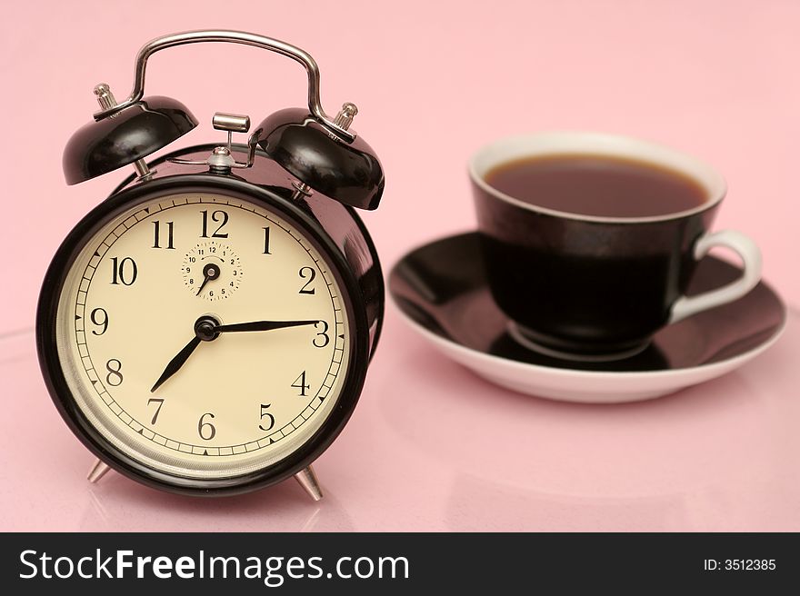 The black alarm clock and black cup from coffee is on a pink background