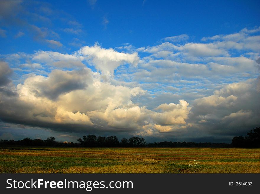 Cloudscape with grassy field in late afternoon.