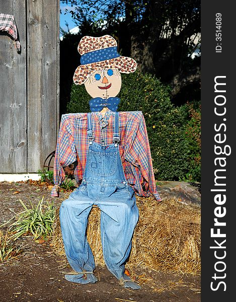 Scarecrow sitting on a bale of hay.