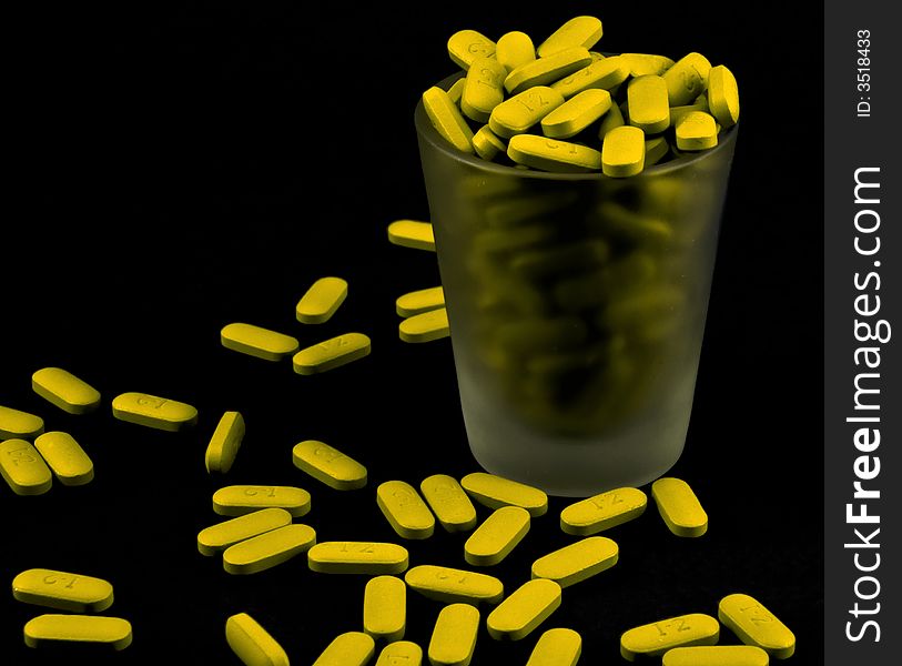 Yellow pills spilling out of a shot glass. Yellow pills spilling out of a shot glass