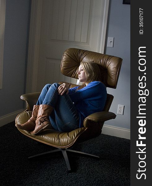 Depressed and sad looking blonde female sitting curled up in a chair, gazing out a window and looking sad. Depressed and sad looking blonde female sitting curled up in a chair, gazing out a window and looking sad.