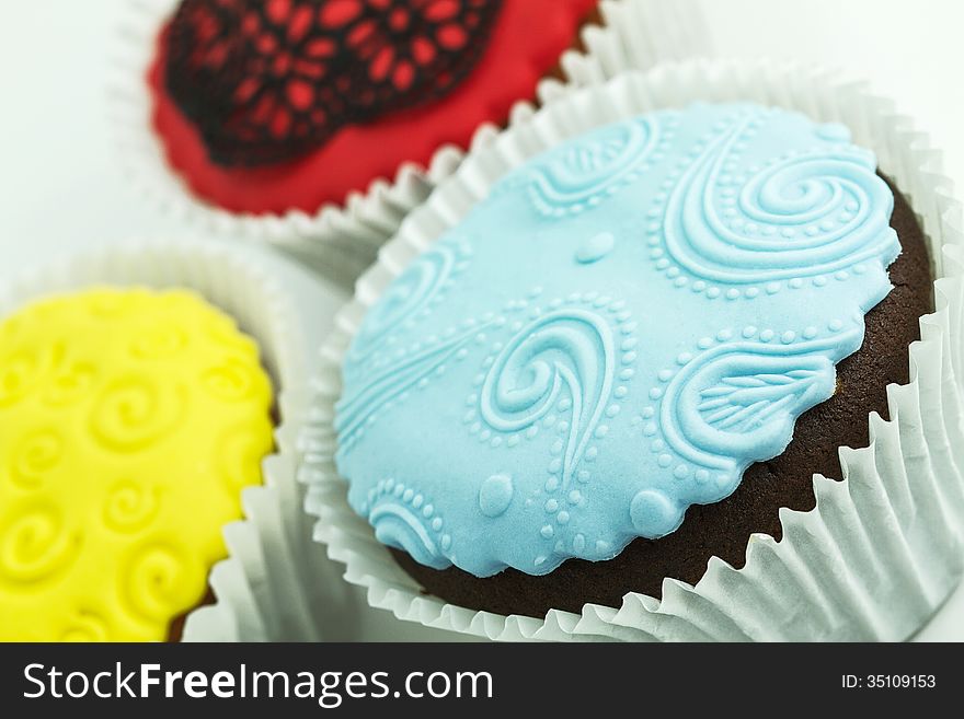 Three cupcakes on the white background. Yellow, blue and red with handmade decoration