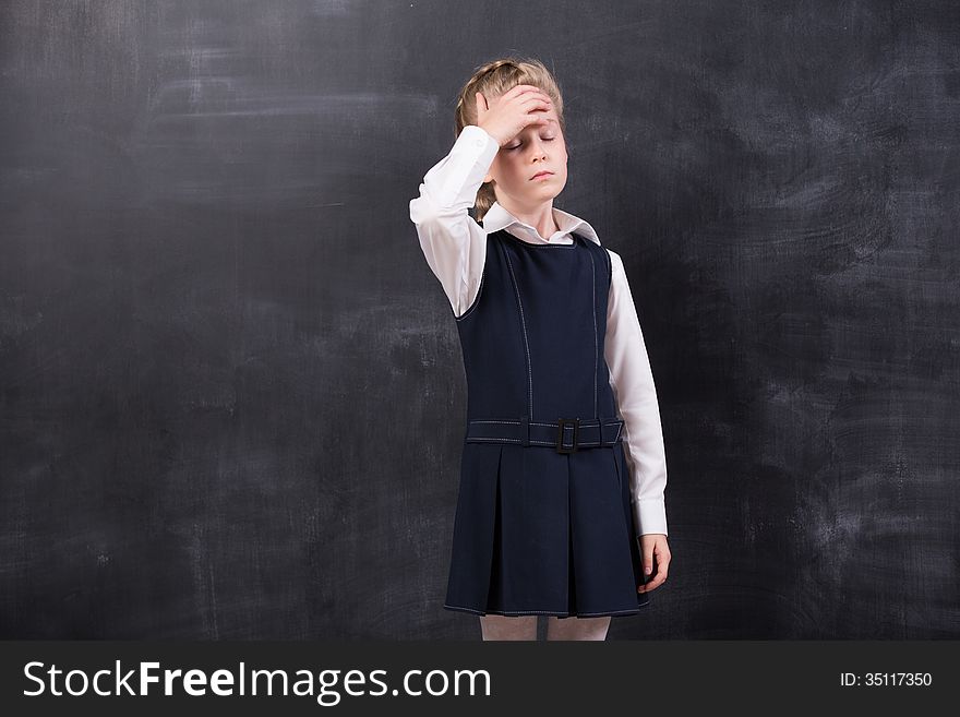 Little schoolgirl with headache holding her head with hands stands at the blackboard. Little schoolgirl with headache holding her head with hands stands at the blackboard