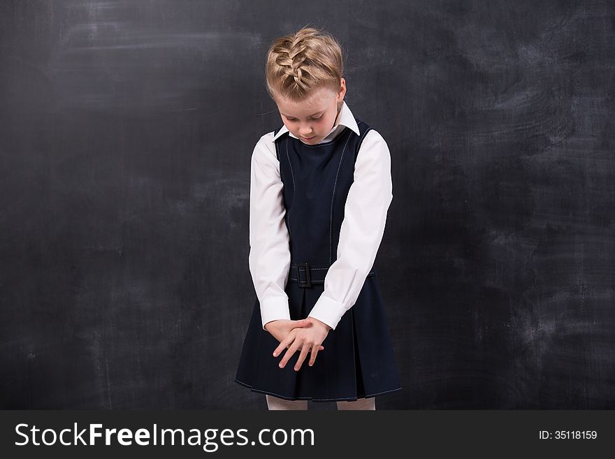 Sad little schoolgirl near blackboard