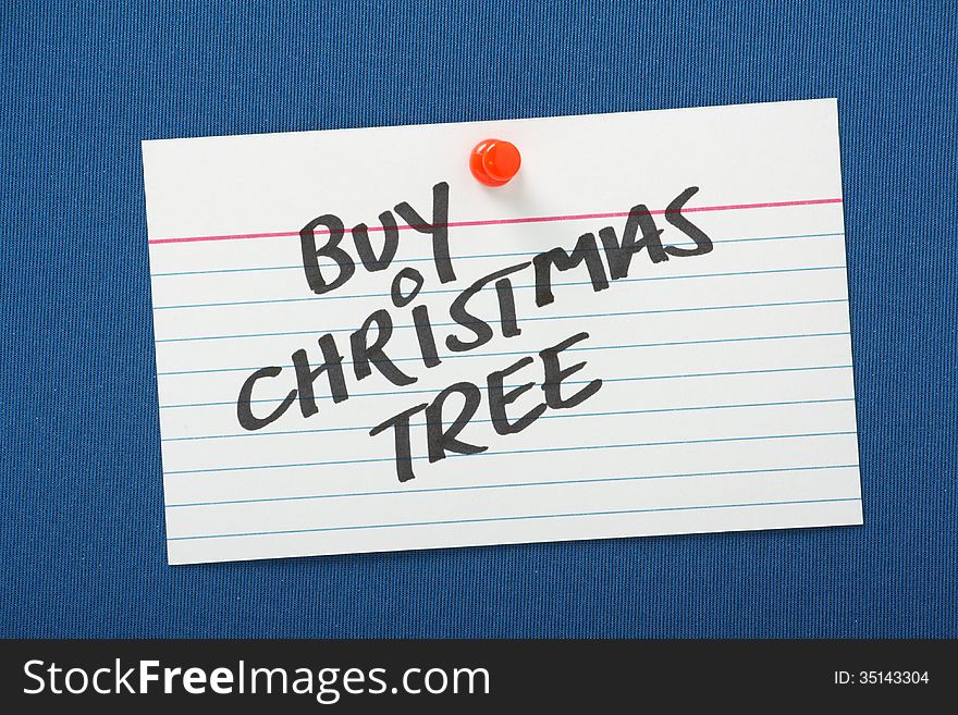 A reminder to buy a Christmas Tree written on a white note card pinned to a blue notice board. A reminder to buy a Christmas Tree written on a white note card pinned to a blue notice board.