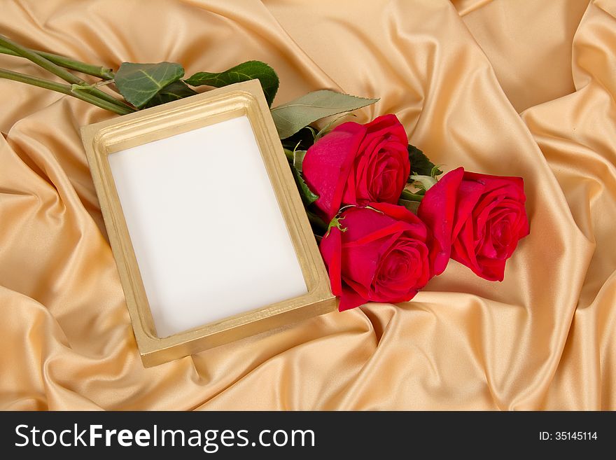 Empty photoframe with a bouquet of red roses on gold fabric