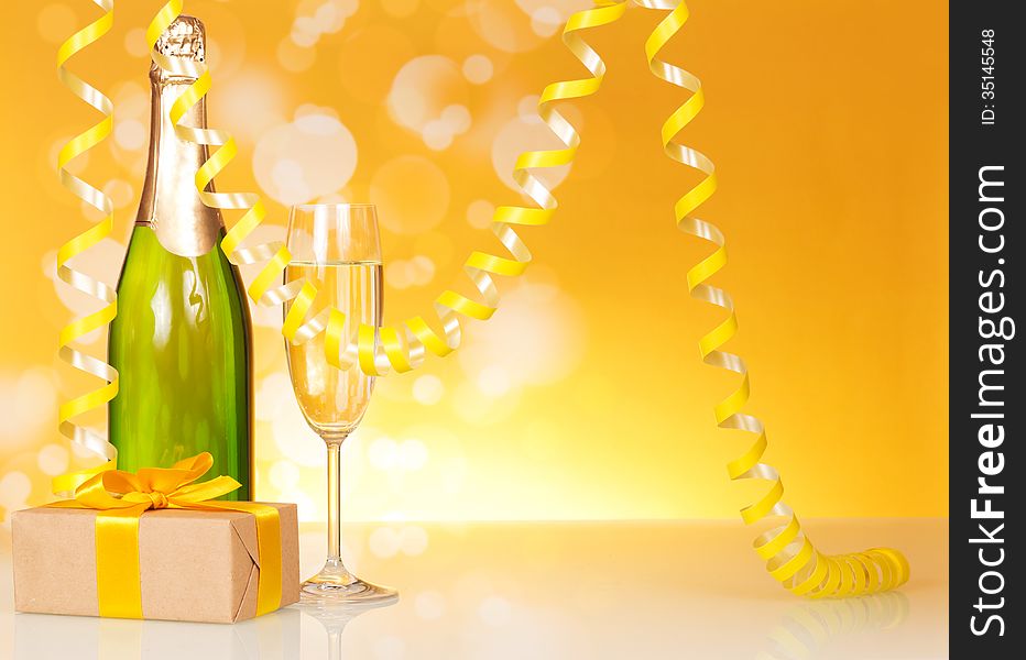 Champagne, glass, gift and serpentine on an abstract yellow background