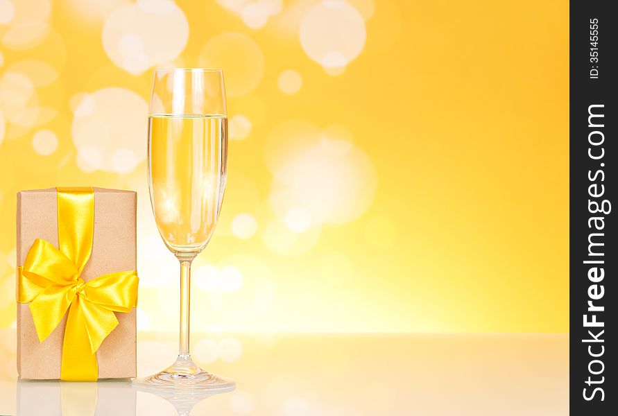 Glass of champagne and gift on an abstract yellow background