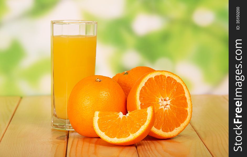 Orange juice on a wooden table against green foliage