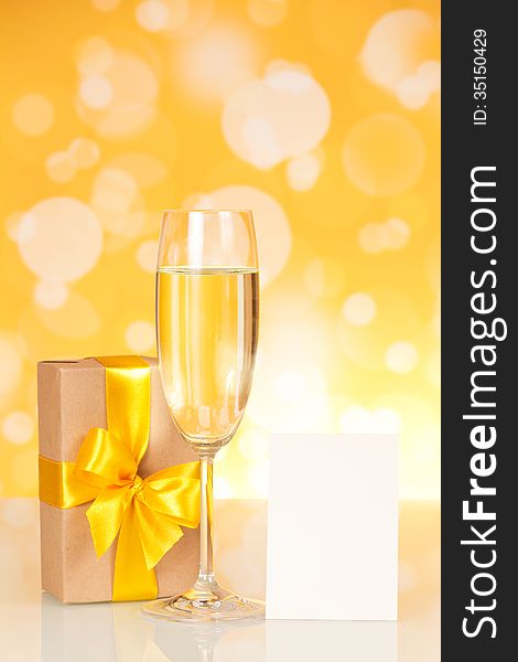 Glass with champagne, a gift and an empty card on an abstract yellow background. Glass with champagne, a gift and an empty card on an abstract yellow background