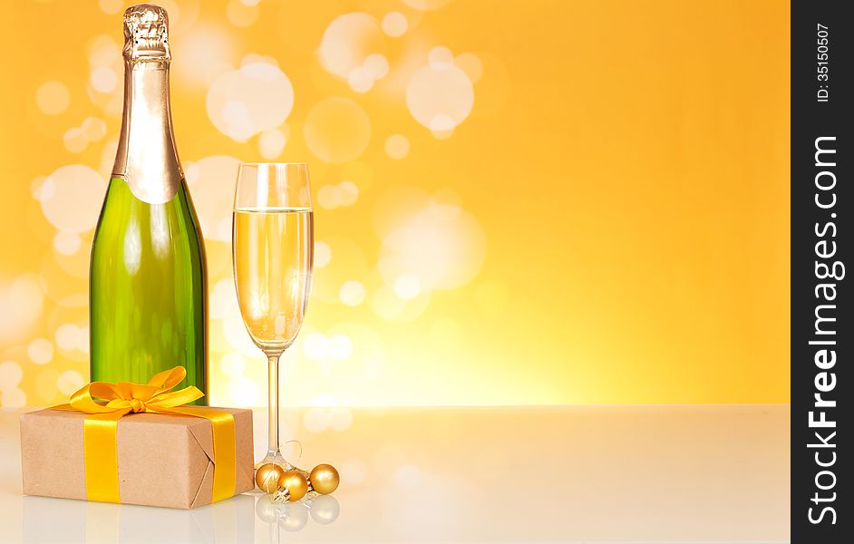 Champagne bottle, glass and gift on an abstract yellow background