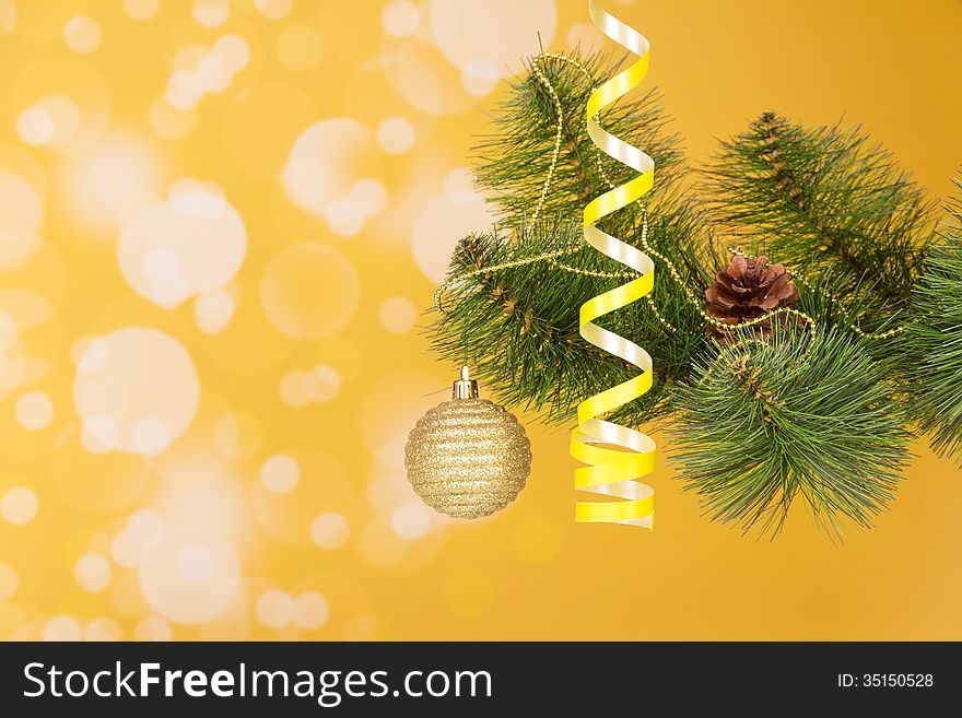 Branch of a Christmas fir-tree with ornament on an abstract yellow background