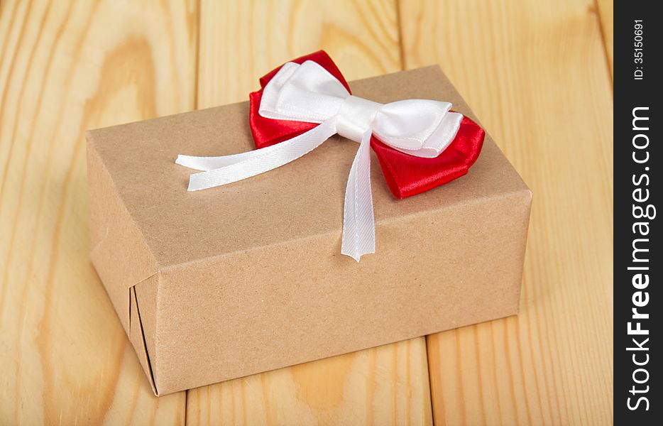 Box from a brown paper with a red-white bow on a wooden surface. Box from a brown paper with a red-white bow on a wooden surface