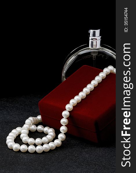 Pearl necklace lies on a red box and a bottle of toilet water