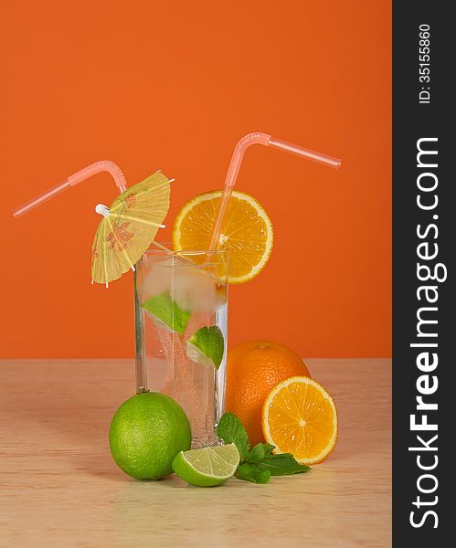 Drink in a glass with straw, is decorated with an umbrella and an orange slice, a juicy lime, on a table. Drink in a glass with straw, is decorated with an umbrella and an orange slice, a juicy lime, on a table