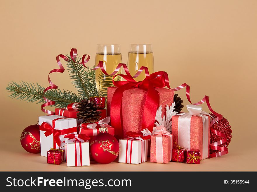 Gift boxes, Christmas toys, pine cones, serpentine and wine glasses with champagne on a beige background