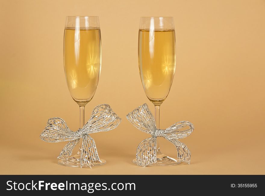 Two glasses with the champagne, decorated silver ribbons on a beige background