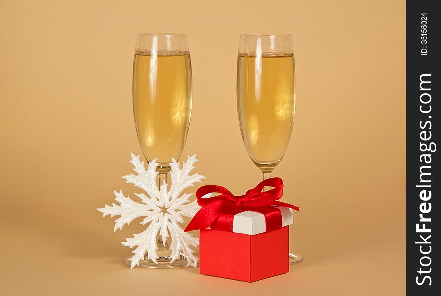 Wine glasses with champagne, a red gift box with a bow and a snowflake on a beige background