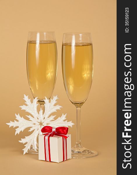 Wine glasses with champagne a beautiful gift box with a bow and snowflake on a beige background