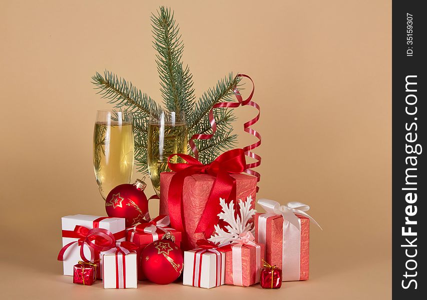 Gift boxes, toys, Christmas tree, serpentine, snowflake and wine glasses with champagne on a beige background