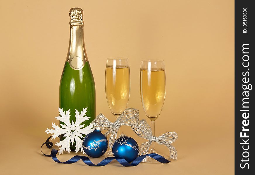 Bottle of champagne, and wine glasses with a silver ribbon, Christmas toys, a snowflake and a serpentine on a beige background. Bottle of champagne, and wine glasses with a silver ribbon, Christmas toys, a snowflake and a serpentine on a beige background