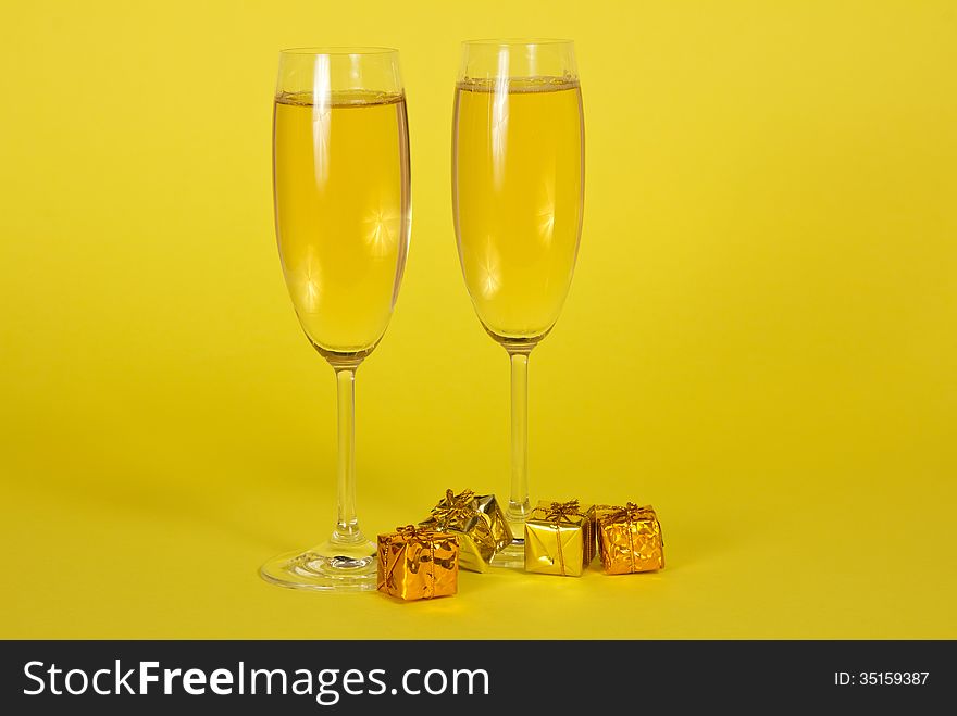 Two wine glasses with champagne and small bright gift boxes on a yellow background