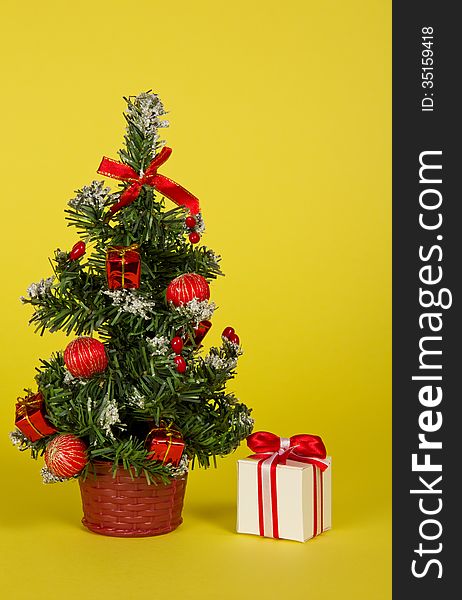 Small fir-tree in a pot with toys and gifts on a yellow background