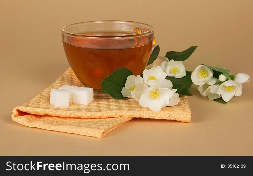 Cup of tea a sugar a branch of a jasmine and a napkin on a beige background. Cup of tea a sugar a branch of a jasmine and a napkin on a beige background