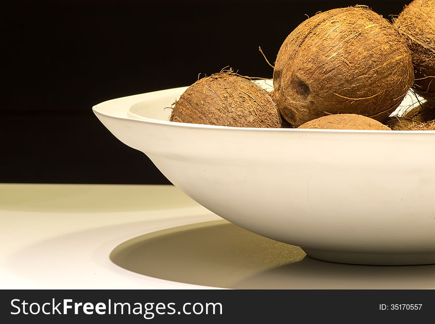 White Bowl of Coconuts on Table with Black Background. White Bowl of Coconuts on Table with Black Background