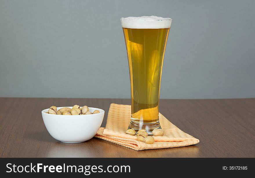 Glass of beer, bowl with pistachios and a napkin on a gray background