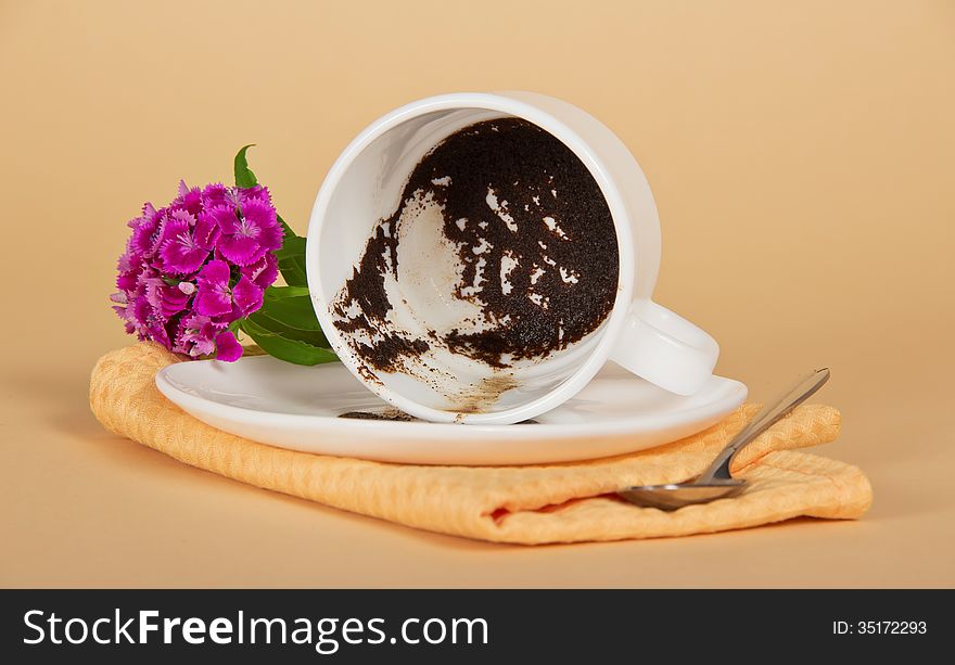 Coffee thick, in the overturned cup, a branch carnation, teaspoon and napkin on a beige background