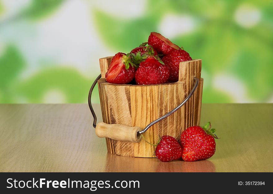 Wooden bucket of ripe fragrant strawberry and two berries near on a table