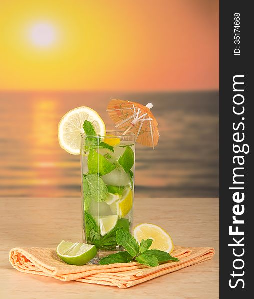 Mojito with umbrella, a lemon, napkin on a table against the sunset. Mojito with umbrella, a lemon, napkin on a table against the sunset