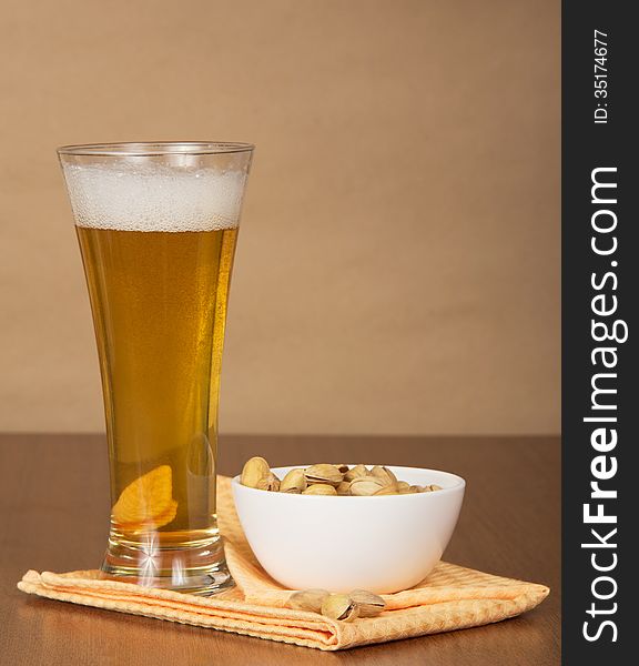 Glass of beer, bowl with pistachios and a napkin against paper. Glass of beer, bowl with pistachios and a napkin against paper