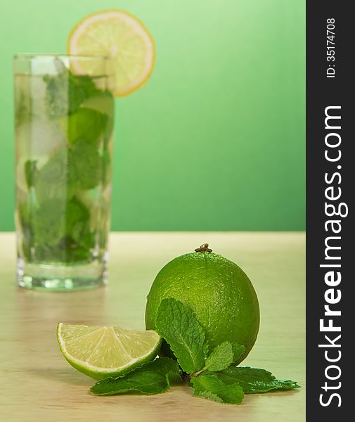 Mojito cocktail, slice of a lemon, and spearmint leaves, on a green background