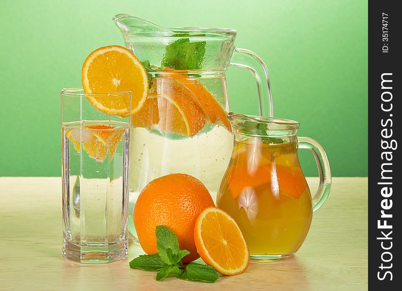 Jugs with drinks and a glass, oranges and spearmint on a table. Jugs with drinks and a glass, oranges and spearmint on a table
