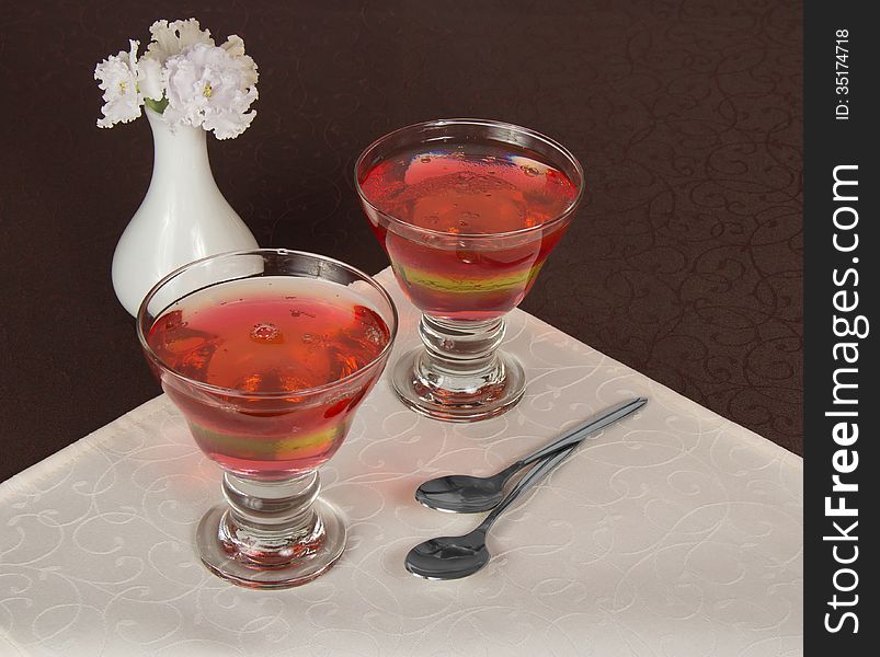 Two glasses with the jelly, two teaspoons and a vase with the flowers on a napkin
