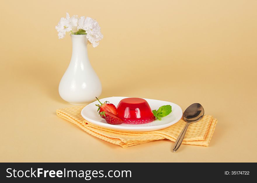 Plate with jelly and a spoon on a napkin, a vase with the flowers, on a beige background. Plate with jelly and a spoon on a napkin, a vase with the flowers, on a beige background