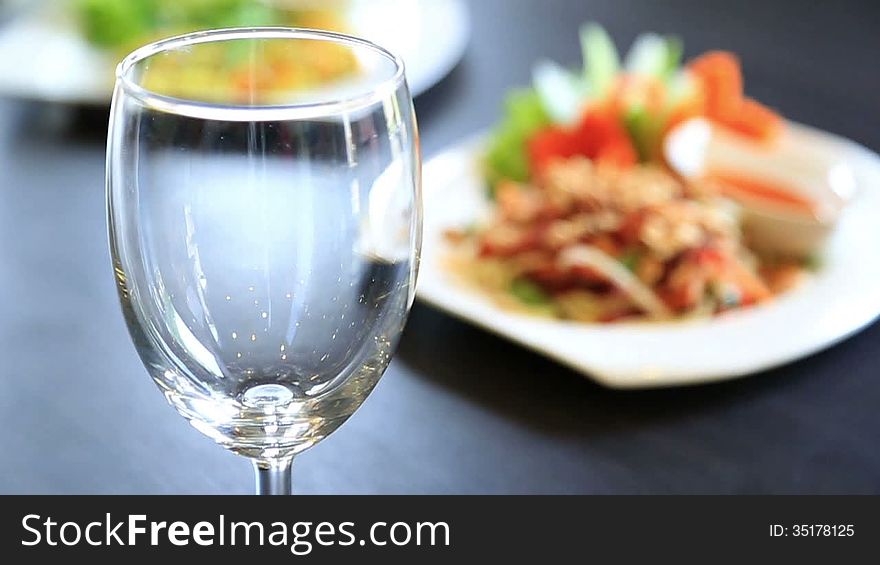 Pouring drinking water into wine glass with food in background