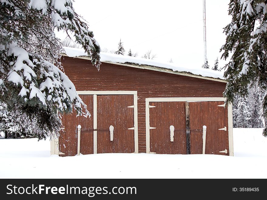 A brown shed between trees and surrounded by snow. A brown shed between trees and surrounded by snow