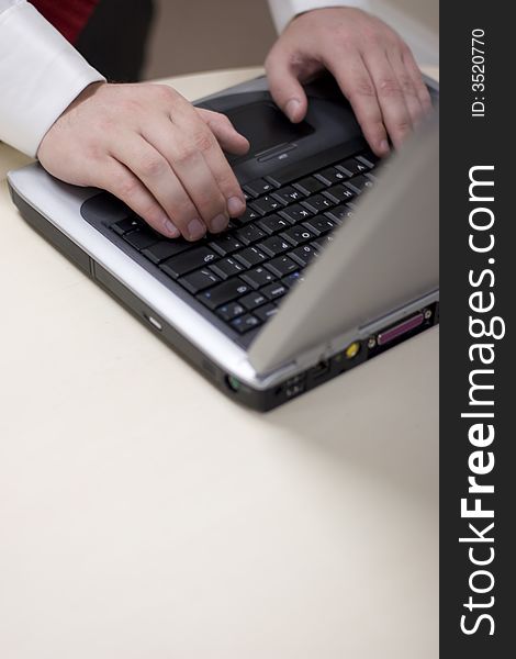 Close up shot of young man's hands typing on keyboard of laptop resting on white table