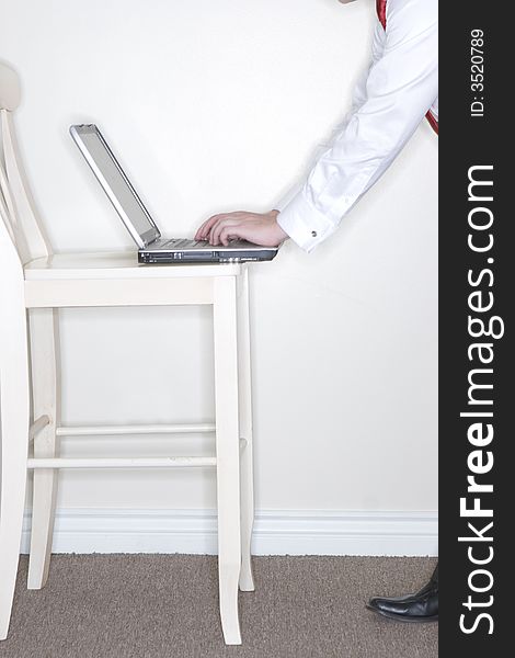 Side view of young man's hands typing on laptop which is resting on white wooden chair