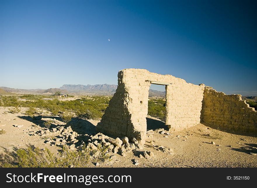 Adobe ruins with mountains and the moon slightly visible in the big blue backdrop of sky. Adobe ruins with mountains and the moon slightly visible in the big blue backdrop of sky.